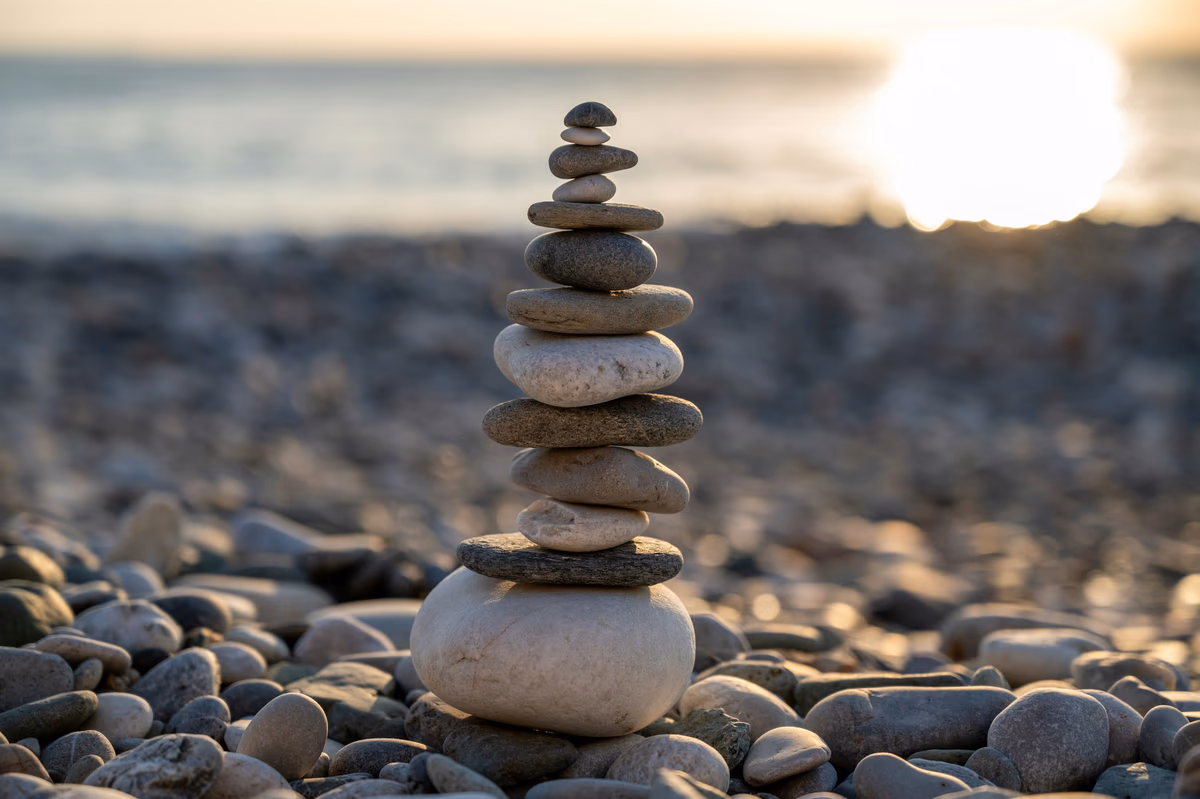 A stack of smooth stones balanced on a pebble beach at sunset