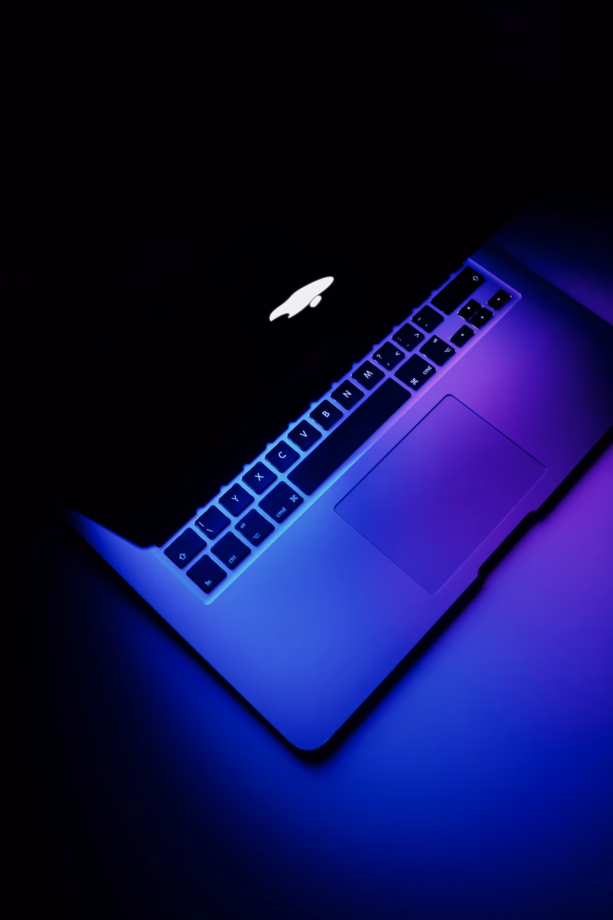 A MacBook with a glowing keyboard on a dark surface, representing the Spendify web app coming alive on desktop